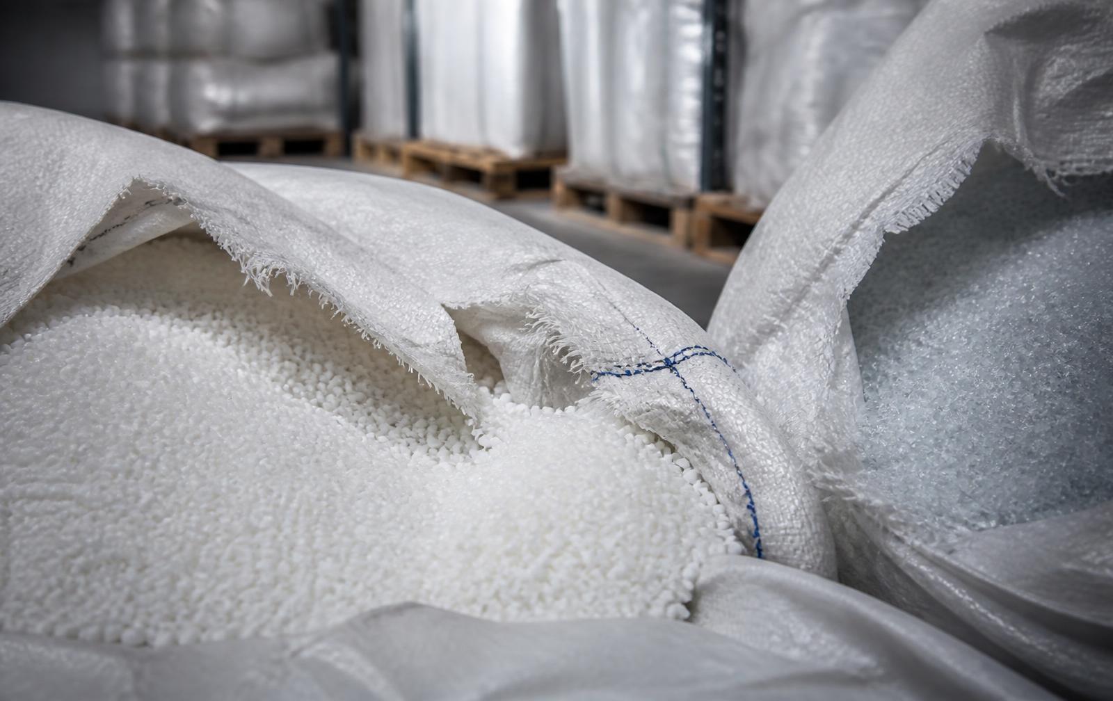 Torn industrial big bags of white polymer granules stored on pallets in a warehouse