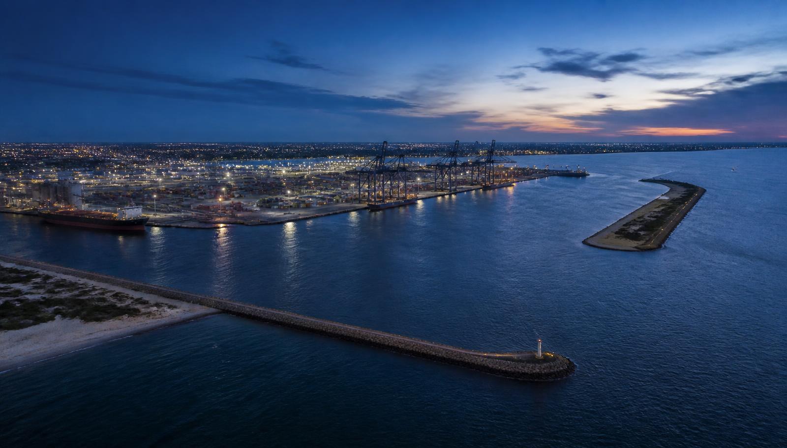 Aerial view at dusk of a large subtropical container and bulk harbour with unbranded gantry cranes, container stacks and a plain bulk carrier at berth