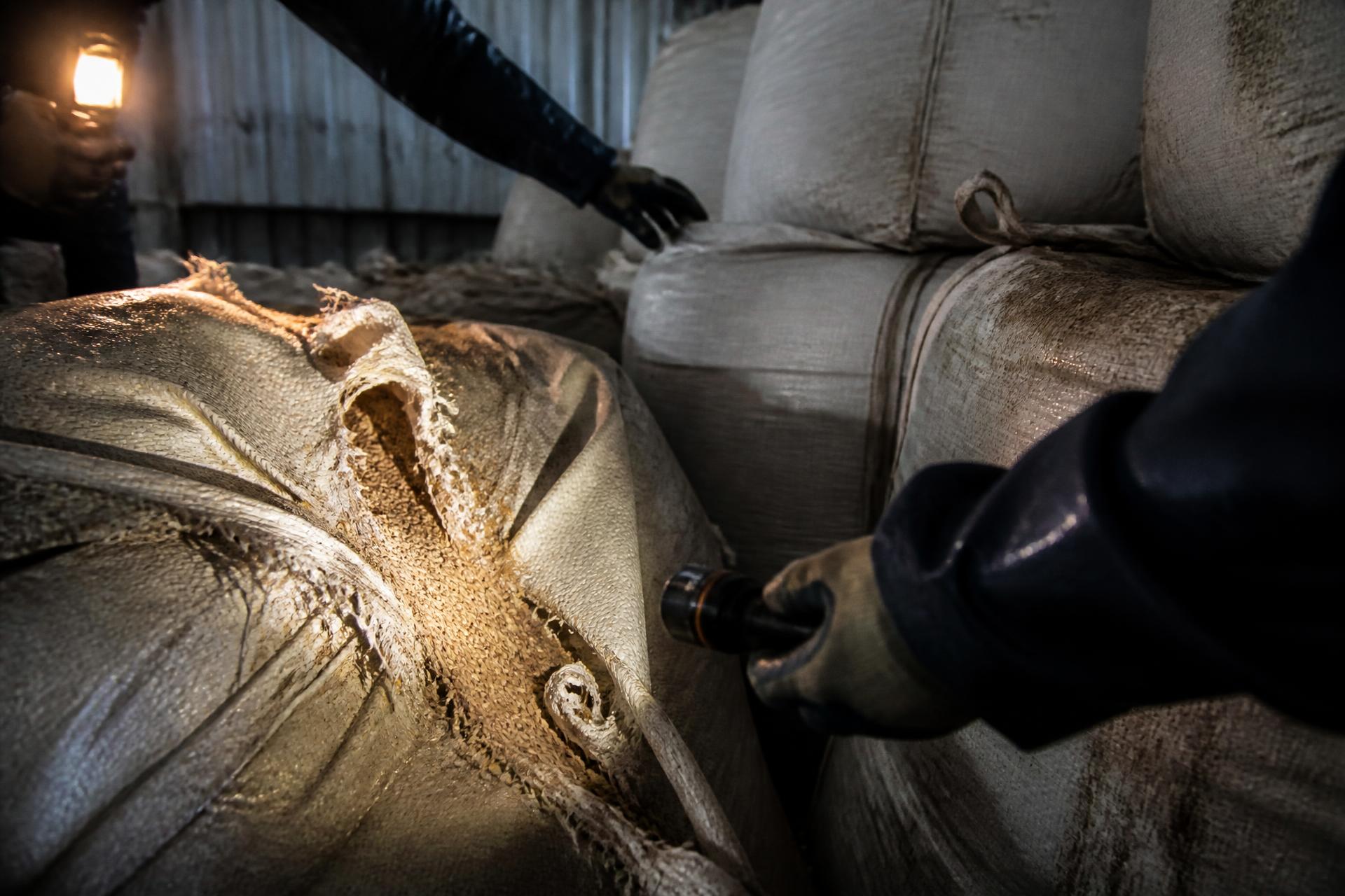 Torn bulk bags with spilled cargo being inspected under a work light